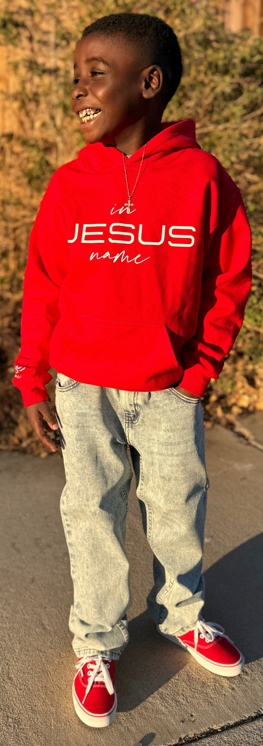 Child wearing a red hoodie with 'A Jesus Name' text, standing outdoors on a sidewalk.